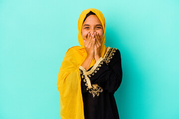 Young muslim woman isolated on blue background laughing about something, covering mouth with hands.