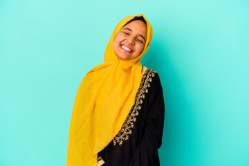 Young muslim woman isolated on blue background relaxed and happy laughing, neck stretched showing teeth.