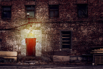 Wall Mural - old brick building at night, dim light over the iron door. gloomy atmosphere and boarded-up windows, a criminal area