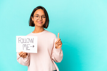 Young hispanic mixed race woman holding a follow me placard showing number one with finger.