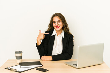 Wall Mural - Young caucasian business woman working on her desktop isolated person pointing by hand to a shirt copy space, proud and confident