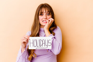 Wall Mural - Young caucasian woman holding a Holidays placard isolated biting fingernails, nervous and very anxious.