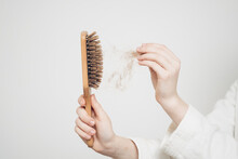 Woman Removes A Bun Of Hair With A Wooden Comb On A Light Background Health Problems Loss
