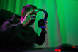© snedorez - Gamer or streamer in headphones with microphone sits at home in neon light and plays at pc