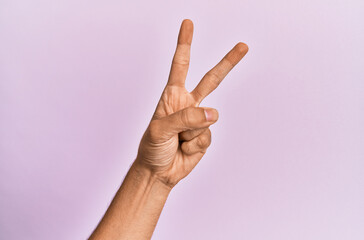 Arm and hand of caucasian young man over pink isolated background counting number 2 showing two fingers, gesturing victory and winner symbol