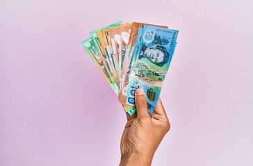 Hispanic hand holding australian dollars banknotes over isolated pink background.