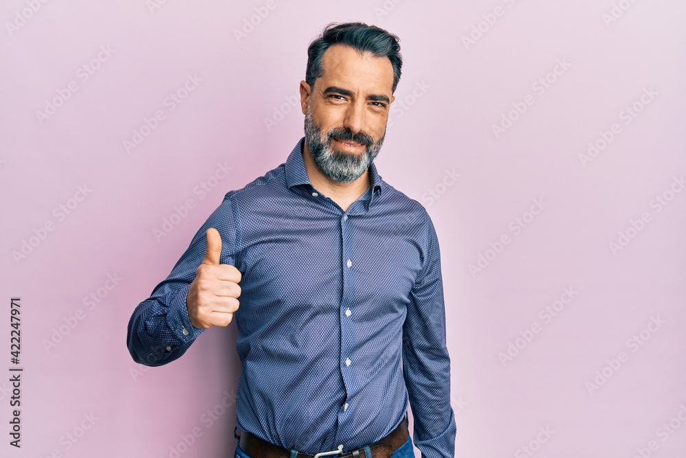 Middle age man with beard and grey hair wearing business clothes doing happy thumbs up gesture with hand. approving expression looking at the camera showing success.