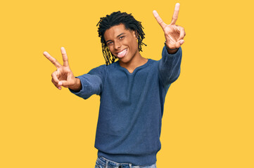 Wall Mural - Young african american man wearing casual winter sweater smiling with tongue out showing fingers of both hands doing victory sign. number two.