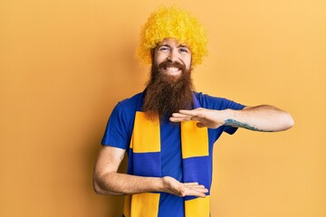 Poster - Redhead man with long beard football hooligan cheering game wearing funny wig gesturing with hands showing big and large size sign, measure symbol. smiling looking at the camera. measuring concept.