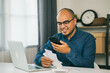 © Chanakon - A young man is using a smartphone to scan the bill to calculate his income and expenses. In his hand there were bills to pay a lot in debt.