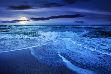 sea tide on a cloudy sunrise. green waves crashing golden sandy beach in full moon light. storm weat