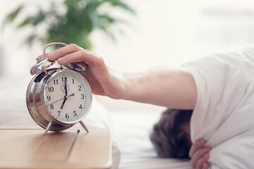 Wall Mural - Alarm clock morning wake-up time on bedside table with man reaching to stop bell