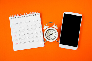 calendar, white alarm clock and mobile phone with clipping part on touch screen on grunge orange background for technology , time passing concept