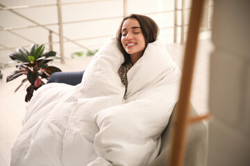 Wall Mural - Beautiful young woman wrapped with soft blanket relaxing on sofa at home