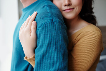 Poster - Cropped image of young woman in love hugging boyfriend from behind when they are standing by window