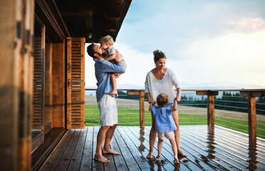 Wall Mural - family with small children playing in rain on patio by wooden cabin, holiday in nature concept.