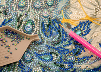 Diamond painting embroidery craft. Acrylic rhinestones and a pen. Closeup, selective focus