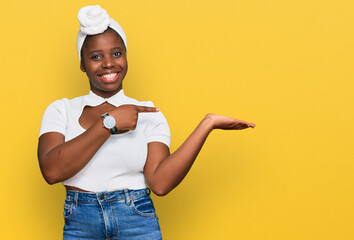 Poster - Young african woman with turban wearing hair turban over isolated background amazed and smiling to the camera while presenting with hand and pointing with finger.