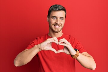 Handsome caucasian man wearing casual red tshirt smiling in love doing heart symbol shape with hands. romantic concept.