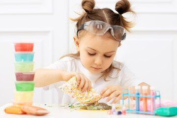 Adorible child in a white T-shirt with two tails in classroom protective glasses and doing experiments, making fluffy slime from multicolored ingredients. Cool kid studying chemistry science