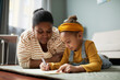 Portrait of cute African-American girl drawing on floor with mother in cozy home interior