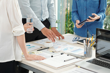 Wall Mural - Group of entrepreneurs standing at table with charts and reports and analyzing statistics data