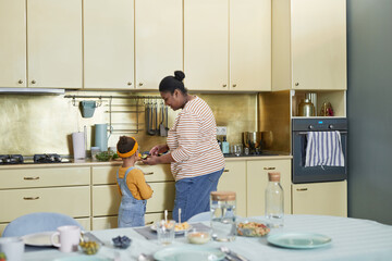 Wall Mural - Back view at happy African-American mother and daughter cooking together in kitchen interior, copy space