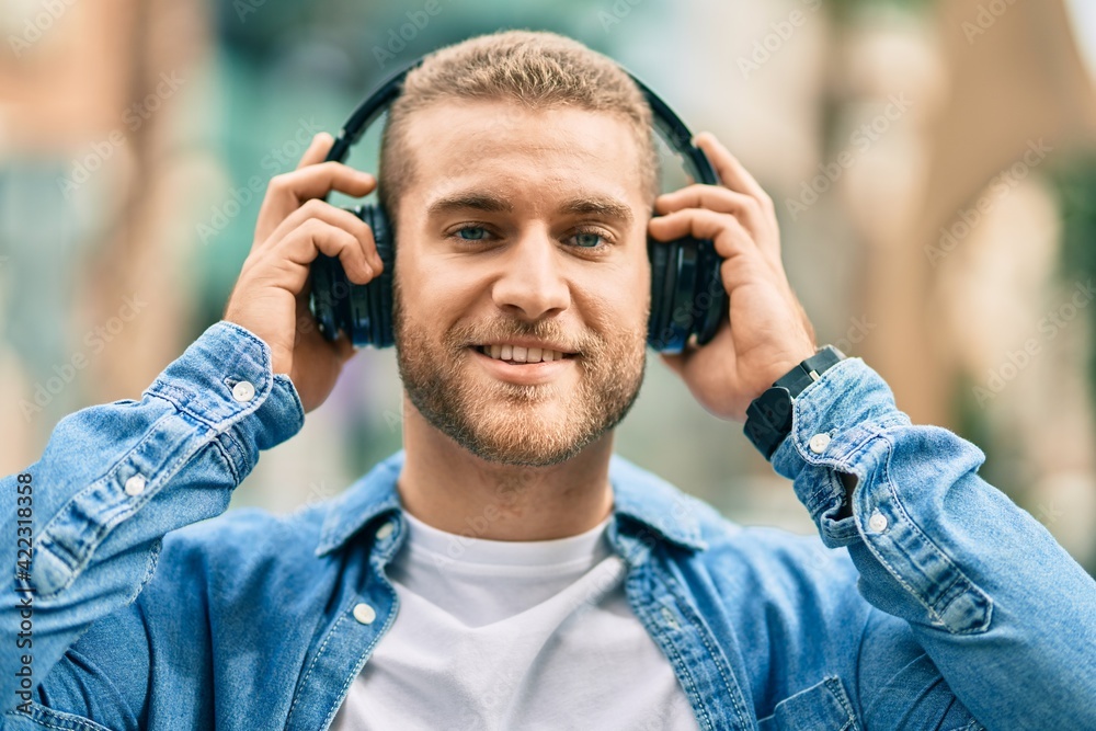 Young caucasian man smiling happy using headphones at the city.