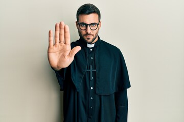 Canvas Print - Young hispanic man wearing priest uniform standing over white background doing stop sing with palm of the hand. warning expression with negative and serious gesture on the face.