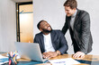 © Kateryna - Happy business people discussing work questions in office, using laptop, developing a new project together. African american male employee asking an advice from caucasian man colleague, smiling