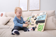 Cute Little Boy Playing With Busy Board On Sofa At Home
