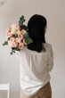 © Natalia - brunette girl in a white shirt with a bouquet of flowers on her shoulder on a wall background