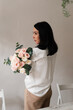 © Natalia - brunette girl in a white shirt with a bouquet of flowers on her shoulder on a wall background