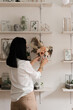 © Natalia - brunette in white shirt decorates the room with flowers vase on the shelf