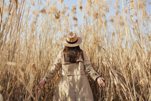 Back View Of Girl In Trench Coat And Hat In Tall Pampas Grass With Blue Sky On The Background.
