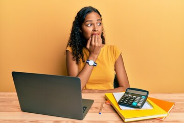 Poster - Young african american girl working at the office with laptop and calculator looking stressed and nervous with hands on mouth biting nails. anxiety problem.