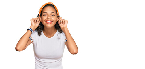 Wall Mural - Young african american girl wearing casual clothes smiling pulling ears with fingers, funny gesture. audition problem