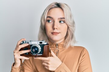 Sticker - Young blonde girl holding vintage camera smiling looking to the side and staring away thinking.