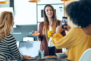 Three smart entrepreneur women talking while taking a break and having a breakfast while taking a photo in the kitchen at coworking place.