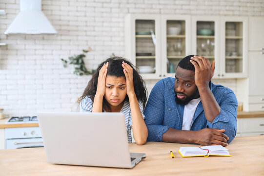 Young African-American couple has financial problem, a frustrated wife and upset husband look through bills on the laptop, young multiracial spouses unable to pay for the mortgage