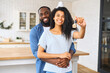 © Vadim Pastuh - Hilarious African-American couple moved in the new house, cheerful beautiful woman in embraces of man is holding key in hand, the newlyweds took the property in a mortgage