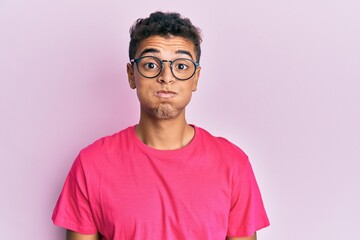 Poster - Young handsome african american man wearing glasses over pink background puffing cheeks with funny face. mouth inflated with air, crazy expression.