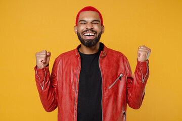 Wall Mural - Young african fun man with funky trendy pink hairdo in stylish red leather jacket black t-shirt do winner gesture clench fist celebrating isolated on yellow orange color background studio portrait