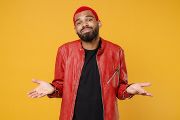 Wall Mural - Young african dark-skinned confused mistaken man 20s with funky trendy pink hairdo wearing red leather jacket spreading hands oops gesture isolated on yellow orange color background studio portrait.