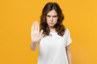© ViDi Studio - Young serious strict angry eueropean caucasian student woman 20s in white basic casual blank print design t-shirt show stop palm gesture refusing isolated on yellow orange background studio portrait.