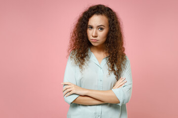 Wall Mural - Young black african american serious arrogant confident shrewd curly woman 20s wearing casual blue shirt holding hands crossed folded looking camera isolated on pastel pink background studio portrait.