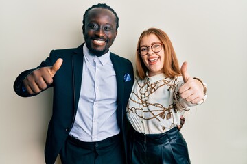 Canvas Print - Young interracial couple wearing business and elegant clothes approving doing positive gesture with hand, thumbs up smiling and happy for success. winner gesture.