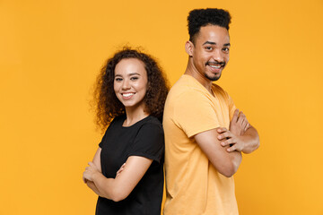 Wall Mural - Young couple friends together team family african smiling happy man woman 20s in black t-shirt stand back to back with hands crossed folded look camera isolated on yellow background studio portrait