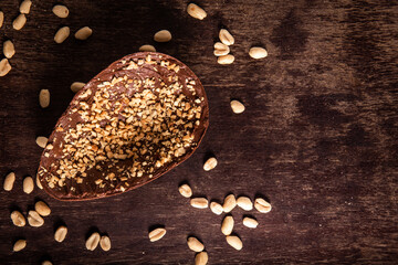 Stuffed chocolate easter egg with peanut and caramel on a wooden table with lots of peanuts around. Top view. Space for text.