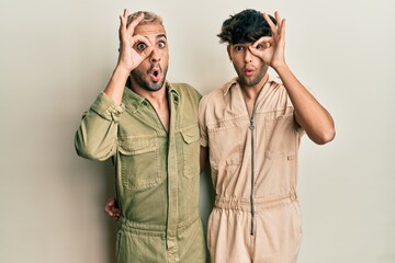 Sticker - Homosexual gay couple standing together wearing casual jumpsuit doing ok gesture shocked with surprised face, eye looking through fingers. unbelieving expression.